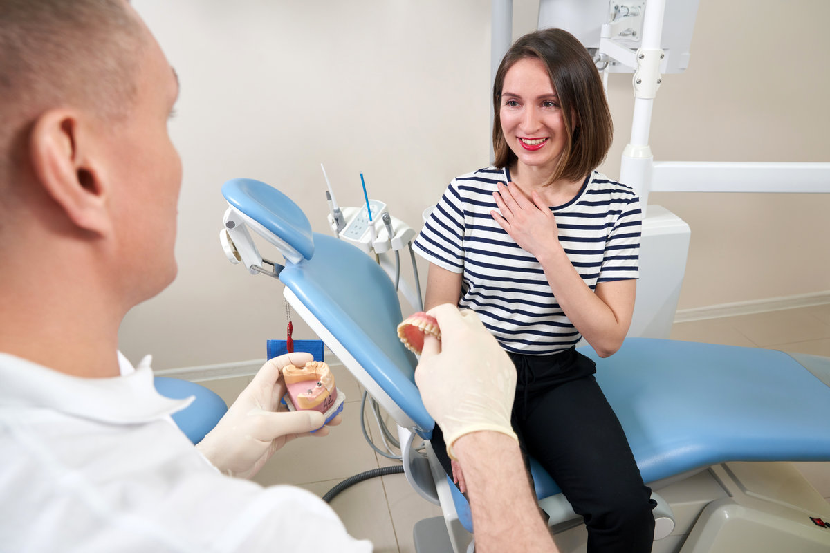 Male dentist showing his female patient a dental implant in modern clinic