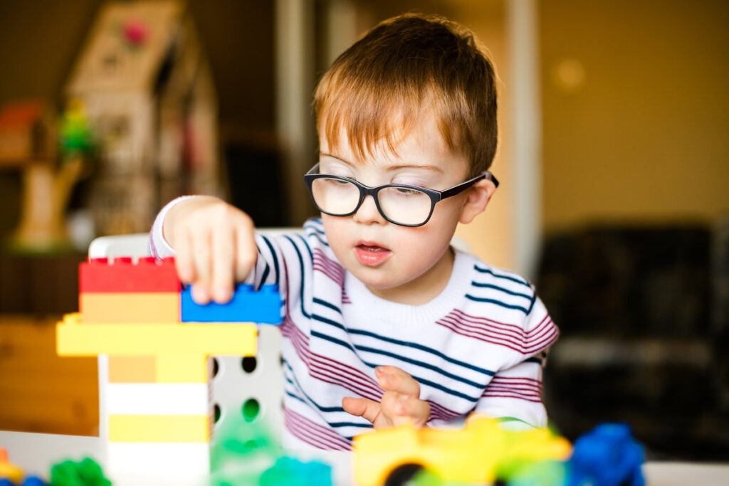 little ginger boy with glasses with syndrome dawn playing with color blocks