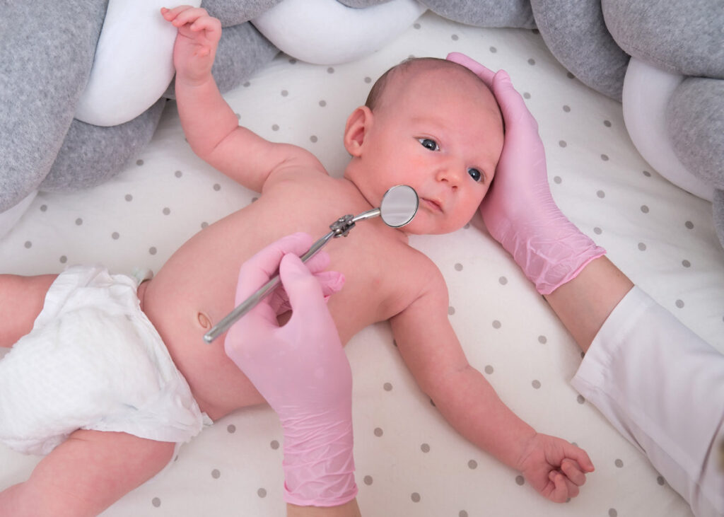 A doctor in uniform checks a child mouth with a mirror. Dentist examines the teeth of a newborn baby