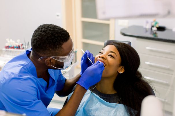 Male african dentist examining a patient with tools in dental clinic.