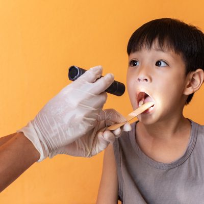 Close up doctor examining throat of patient with tongue depressor.