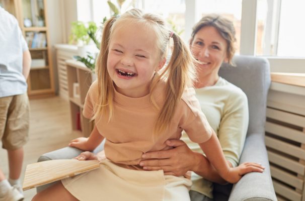 Portrait of cute girl with down syndrome laughing happily while playing with mother at home