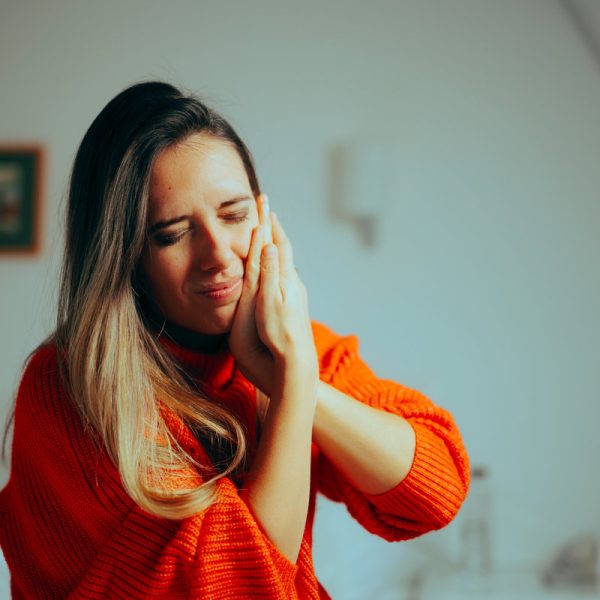 Woman in orange sweater, touching face